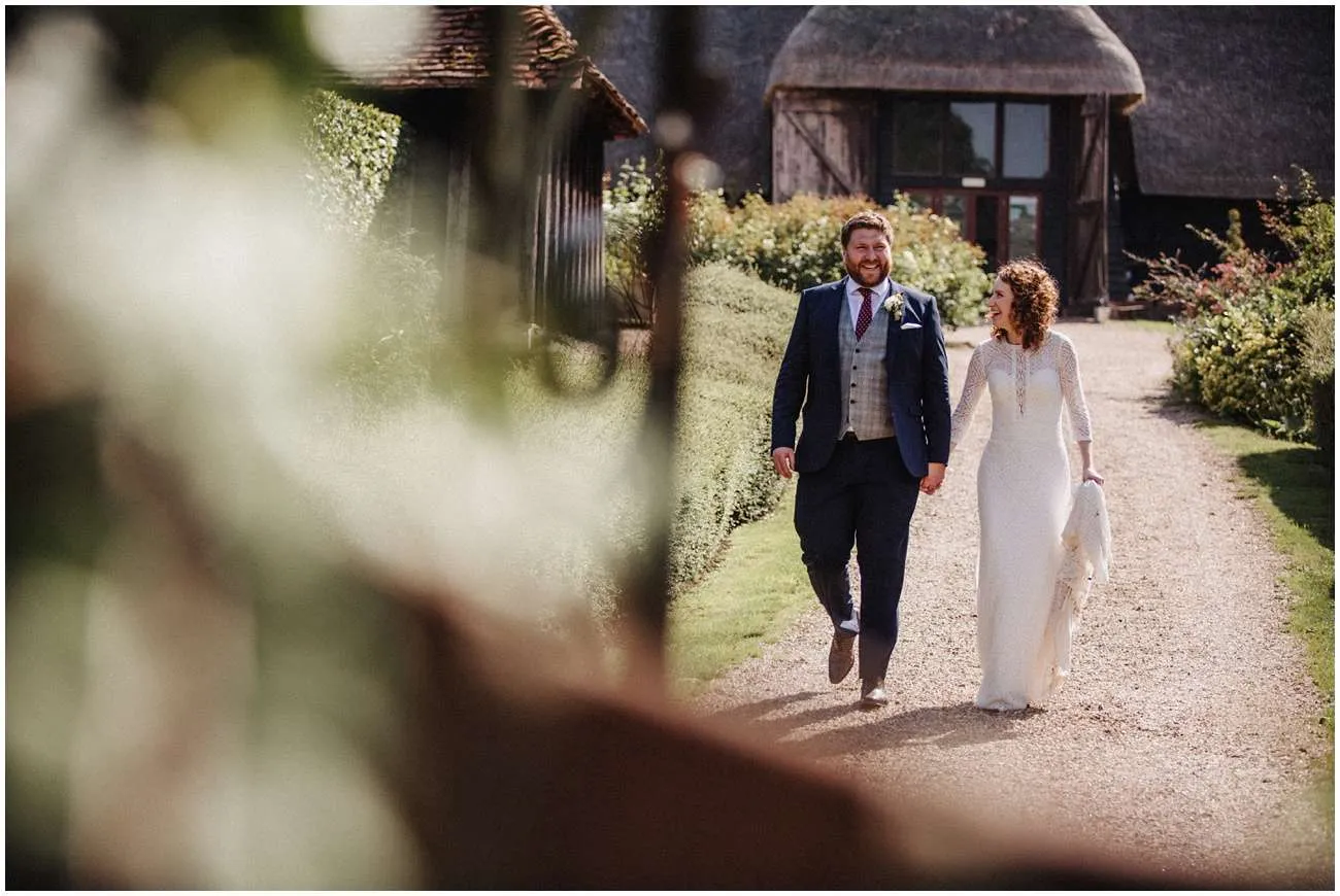 Bride and groom walk holding hands along a gravel path in the sunshine