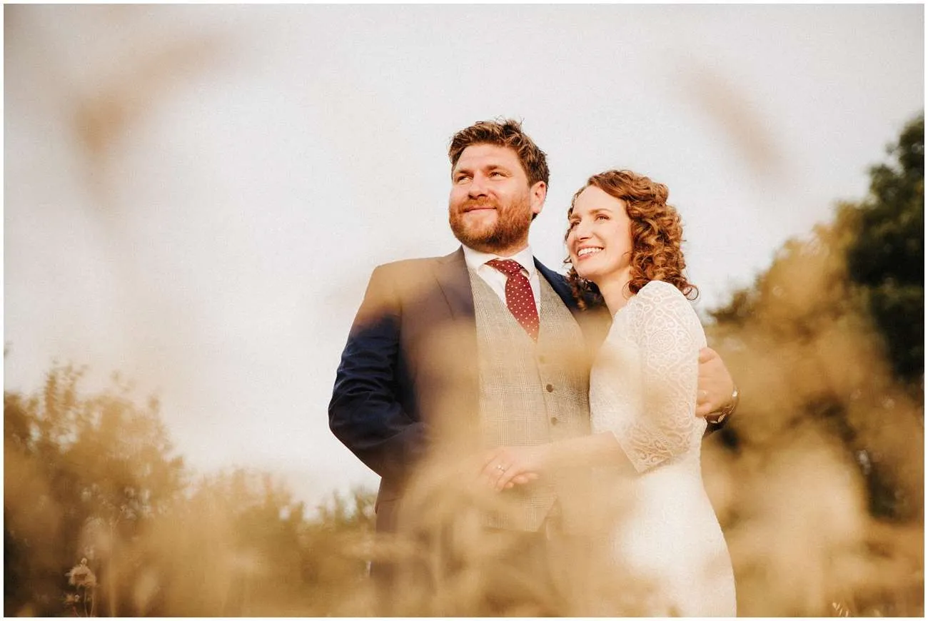 The bride and groom look out over the fields during sunset