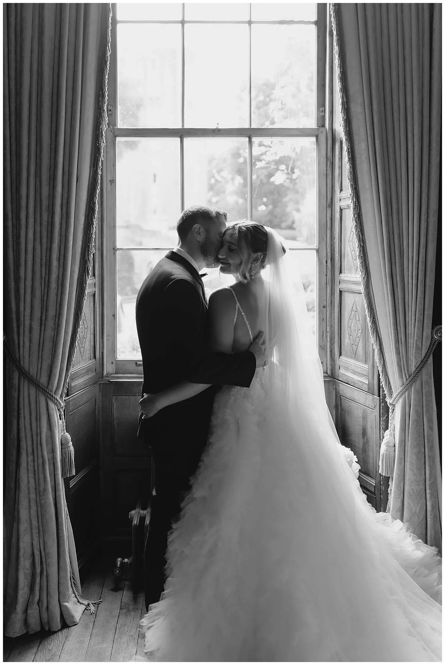 Hedingham Castle Wedding Photographer - a tender embrace of the bride and groom by a large window