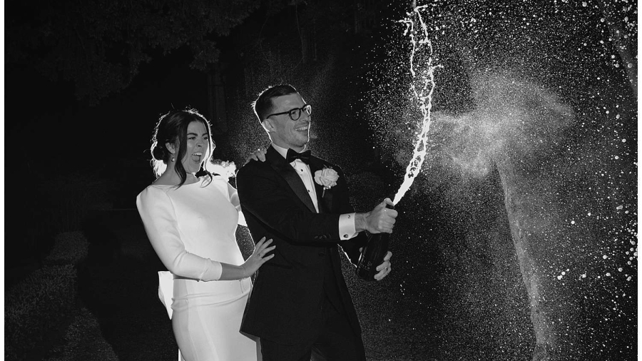 Mulberry House Wedding Photographer - The bride and groom spray champagne at night at the front of the venue