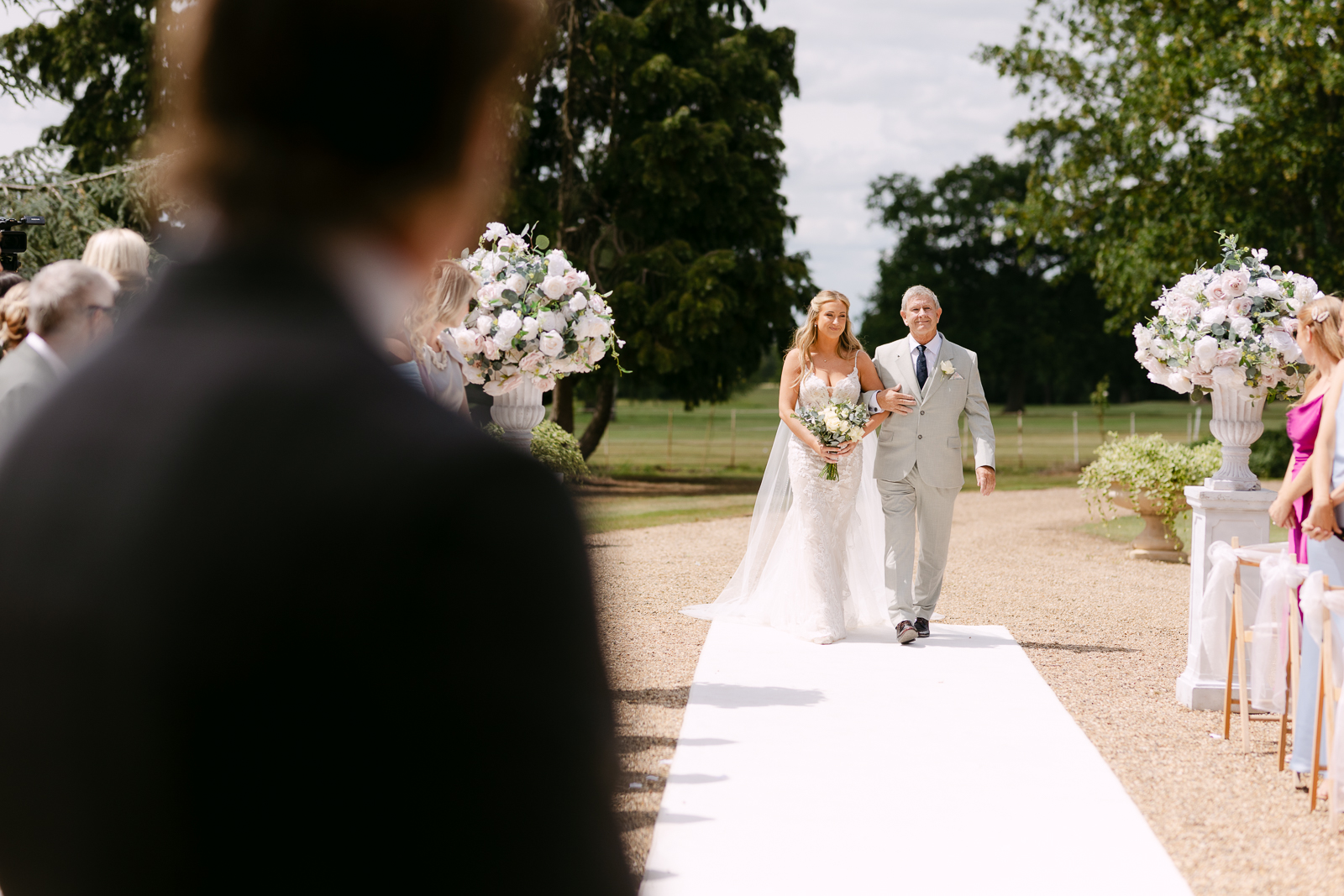 Molly walking down the aisle with her dad during an outdoor Gosfield Hall courtyard ceremony