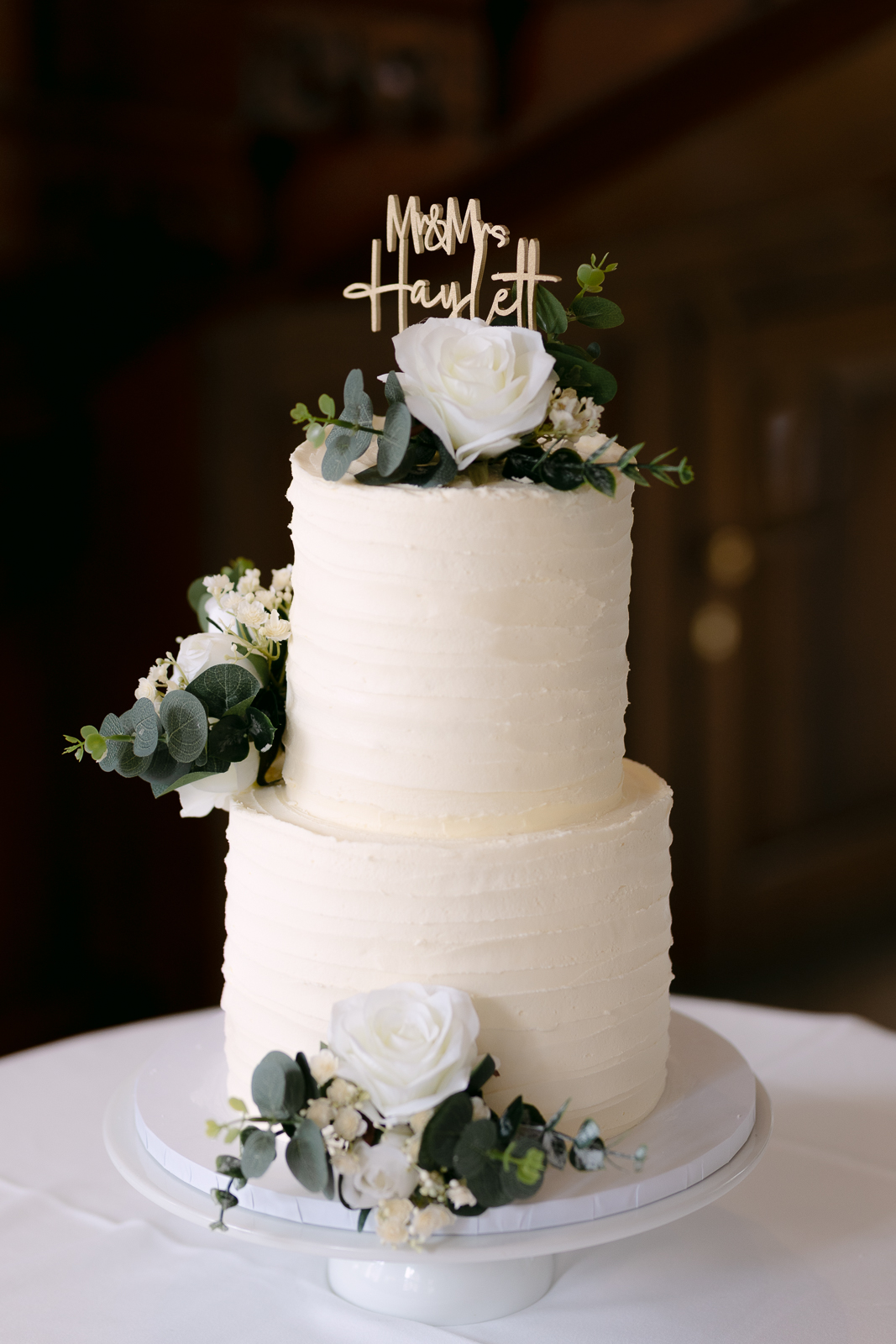 Molly and Taylor's white wedding cake decorated with roses and eucalyptus at Gosfield Hall